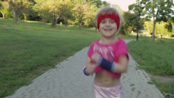 Pequeña niña corredora caucásica en ropa deportiva rosa corriendo al aire libre en el parque. Entrenamiento para niños — Vídeos de Stock