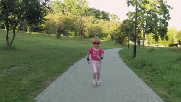 Pembe spor kıyafetleri içinde parkta koşan beyaz bir kız çocuğu. Çocuklar için egzersiz — Stok video