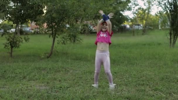 Giovane ragazza bambino carino in abbigliamento sportivo facendo esercizi di salto di forma fisica all'aperto nel parco. Allenamento per bambini — Video Stock