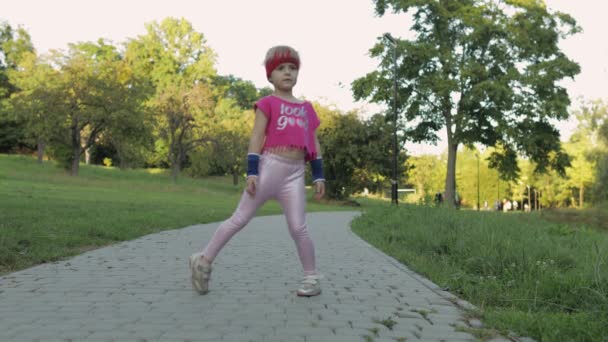 Spor giyim bölümünde, dışarıda parkta spor egzersizleri yapan tatlı bir kız çocuğu. Çocuklar için egzersiz — Stok video
