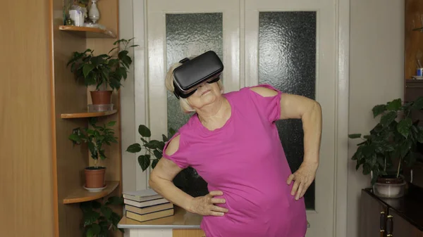 Avó em óculos de fone de ouvido virtual assistindo vídeo em capacete VR e treino em casa — Fotografia de Stock