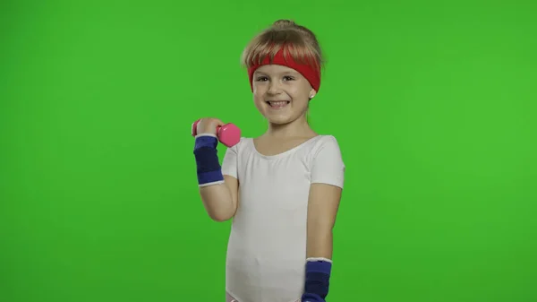 Белая девушка в спортивной одежде делает упражнения с гантелями. Тренировка для детей. Атлетическое дитя — стоковое фото