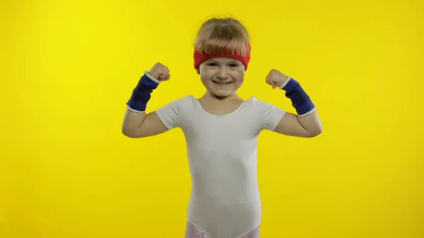 Atletisch meisje in witte sportkleding toont spieren geïsoleerd over gele achtergrond. Workout voor kinderen — Stockfoto