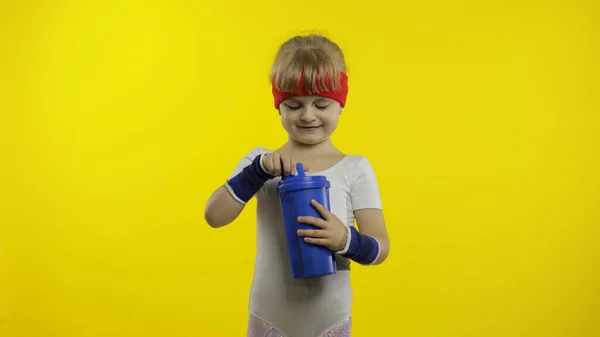 Κορίτσι σε αθλητικά ρούχα πόσιμο νερό για αναψυκτικό μετά από ασκήσεις φυσικής κατάστασης. Μικρό αθλητικό παιδί. — Φωτογραφία Αρχείου