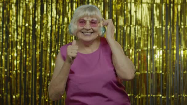Anciana mayor baila, escucha música en los auriculares. Relajarse, disfrutar, divertirse, sonreír — Vídeos de Stock