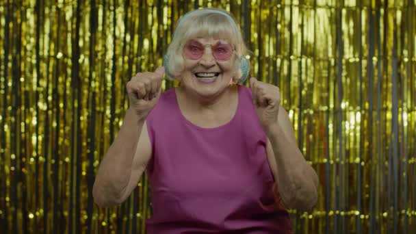 나이든 할머니가 춤을 추고 헤드폰으로 음악을 듣습니다. 휴식, 즐기기, 즐기기, 즐겁게 웃기 — 비디오