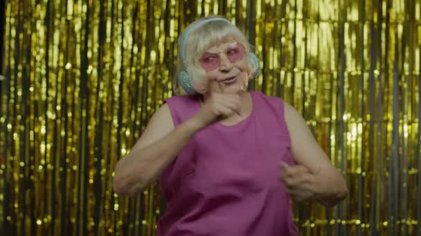 나이든 할머니가 춤을 추고 헤드폰으로 음악을 듣습니다. 휴식, 즐기기, 즐기기, 즐겁게 웃기 — 비디오