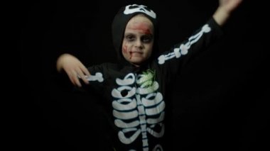 Yüzünde kan makyajı olan kızgın bir Cadılar Bayramı kızı. Korkunç iskelet gibi giyinmiş çocuk, dans ediyor, surat asıyor.