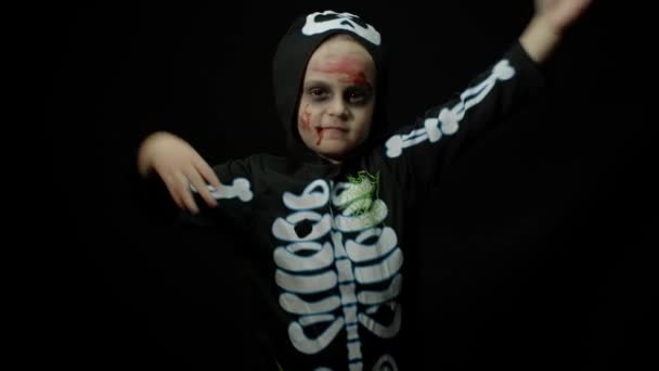 顔に血の化粧をしたハロウィン怒っている女の子。怖い骨格をした子供は踊り顔を作る — ストック動画