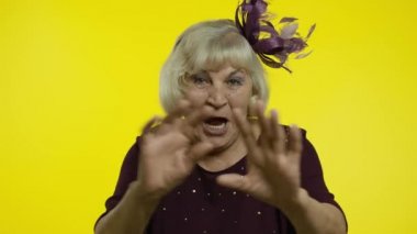 Dost canlısı yaşlı bir kadın el sallıyor kameraya bakıyor dişlek bir gülümsemeyle, selam veriyor, selamlıyor.