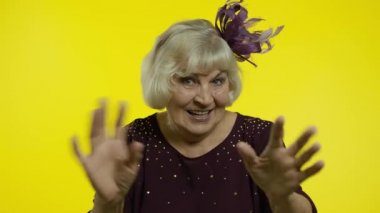 Dost canlısı yaşlı bir kadın el sallıyor kameraya bakıyor dişlek bir gülümsemeyle, selam veriyor, selamlıyor.