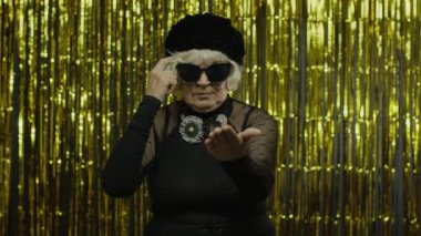 Yaşlı bir kadının aptalca bir jest yapmasından memnun değilim. Sarı arka planda yaşlı büyükanne.