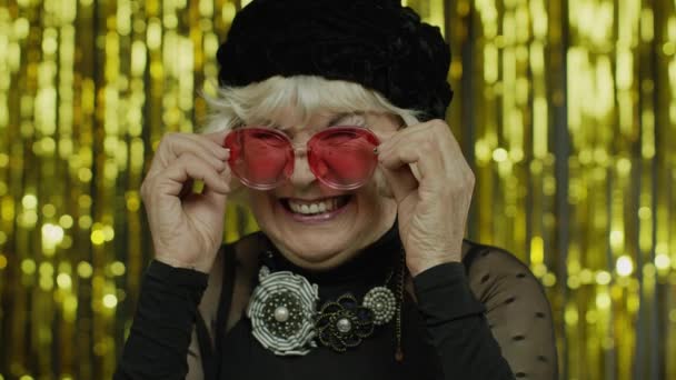 Preciosa anciana madura tocando gafas de sol rojas y guiñando el ojo juguetonamente, coqueteando y parpadeando — Vídeos de Stock