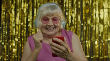 Cep telefonu tutan, kulaklıkla müzik dinleyen ve dans eden mutlu, yaşlı bir kadın.