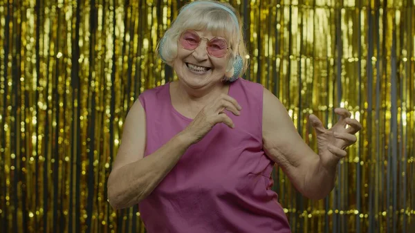 Старша стара жінка танцює, слухає музику на навушниках. Розслабляючись, насолоджуючись, розважаючись, посміхаючись — стокове фото