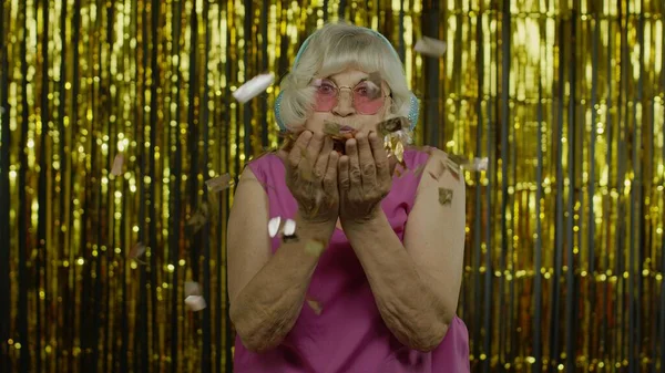 Feliz anciana madura riendo, soplando purpurina de confeti, celebrando cumpleaños, ganando la lotería — Foto de Stock