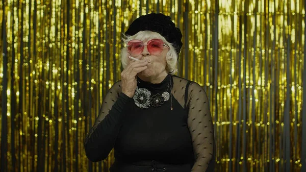 Anciano estilo madura abuela en la moda negro ropa en gafas de sol posando, cigarrillo de humo —  Fotos de Stock