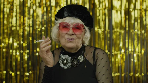 Ältere ältere Geschäftsfrau in modischer schwarzer Kleidung posiert mit Sonnenbrille, raucht Zigarette — Stockfoto