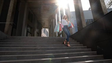 Alışveriş merkezinden alışveriş torbalarıyla yürüyen gülümseyen bir kız, Kara Cuma günü satın almaktan mutlu.