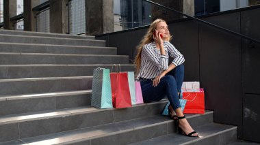 Merdivenlerde oturan ve cep telefonuyla Kara Cuma 'daki alışveriş merkezinde indirimden bahseden bir kız.