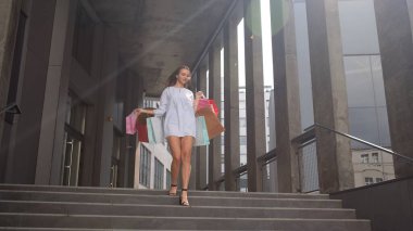 Alışveriş merkezinden alışveriş çantalarıyla yürüyen çekici bir kız, Kara Cuma günü satın almaktan memnun.