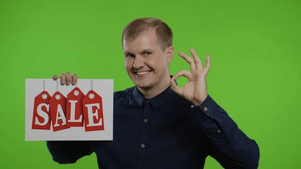 Happy man holding Sale word inscription and showing Ok sign. Guy rejoicing with good sale discounts — Stock Photo, Image