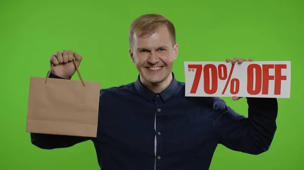 快乐的男人展示购物袋和高达70%的刻字标志。假期折扣优惠 — 图库照片