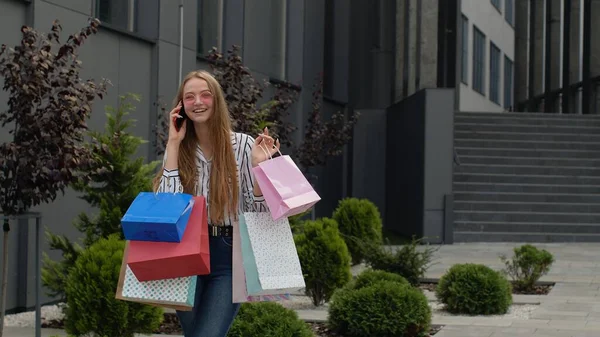 Cep telefonunda çantalı genç kız Kara Cuma 'daki alışveriş merkezindeki satışlar hakkında konuşuyor.