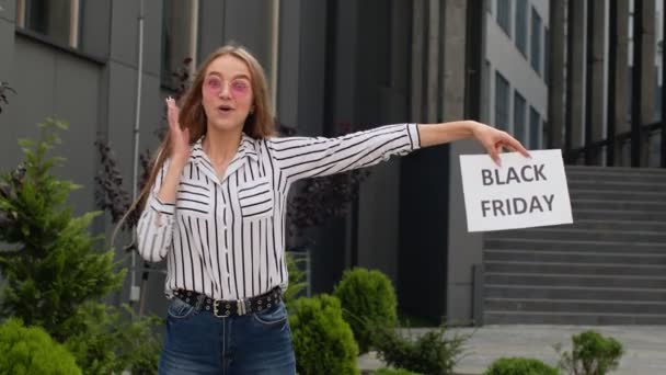 Szczęśliwa dziewczyna trzymająca napis Black Friday i wskazująca na niego. Tło centrum handlowego — Wideo stockowe