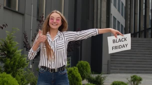 Opgewonden tiener meisje tonen zwarte vrijdag inscriptie, reclame kortingen, tonen duimen omhoog — Stockvideo