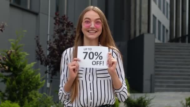 Χαμογελαστό κορίτσι δείχνει μέχρι 70 τοις εκατό Off επιγραφές πινακίδες, χαρά καλές εκπτώσεις, χαμηλές τιμές — Αρχείο Βίντεο
