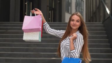 Kız yürüyor ve alışveriş torbaları üzerinde Kara Cuma yazısını gösteriyor, mağazada indirimler var.