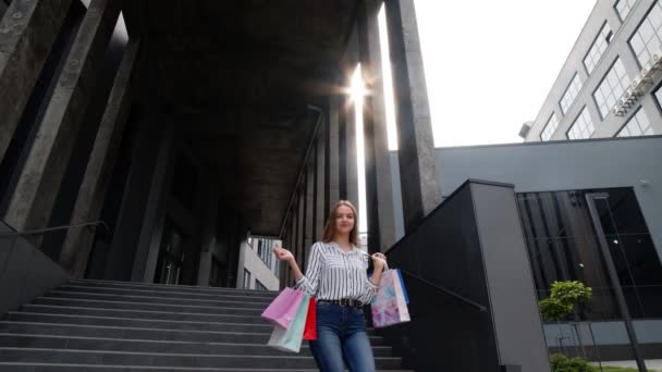 Lächelndes Mädchen läuft mit Einkaufstüten aus dem Einkaufszentrum und freut sich über den Einkauf am Black Friday — Stockvideo