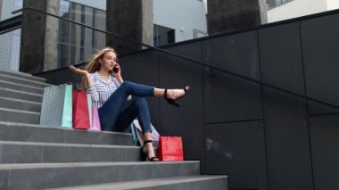 Merdivenlerde çantalarla oturan ve akıllı telefondan Kara Cuma 'daki alışveriş merkezinde satıştan bahseden kız.