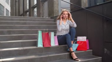 Merdivenlerde oturan ve cep telefonuyla Kara Cuma 'daki alışveriş merkezinde indirimden bahseden bir kız.