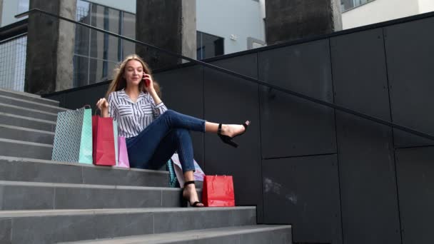 Fille assise sur les escaliers avec des sacs parler sur téléphone mobile à propos de la vente dans le centre commercial Black Friday — Video