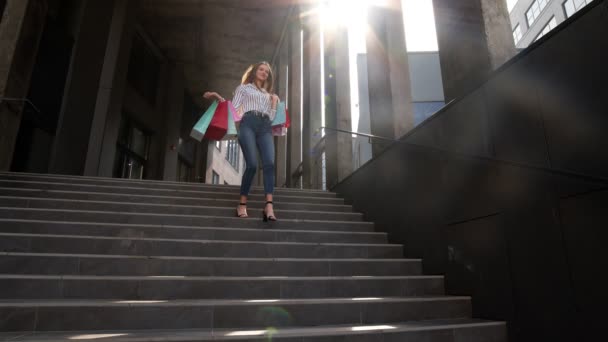 Chica alegre caminando desde el centro comercial con bolsas de compras, feliz con la compra el Viernes Negro — Vídeos de Stock