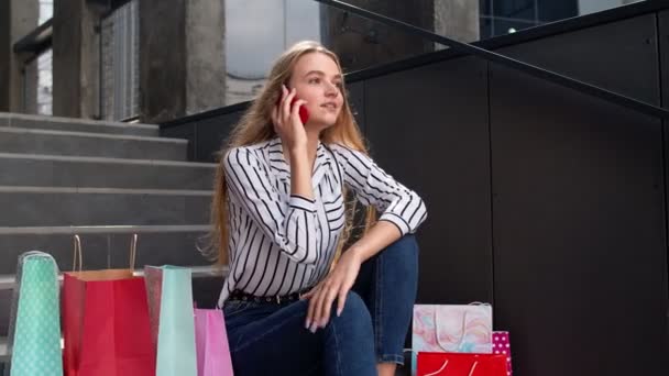 Meisje zit op de trap met tassen praten op mobiele telefoon over de verkoop in het winkelcentrum in Black Friday — Stockvideo