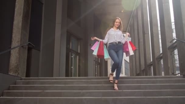 Улыбающаяся девушка, идущая из центра с сумками для покупок, довольна покупками в Черную пятницу — стоковое видео