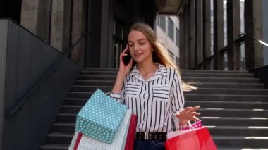 Alışveriş merkezinden alışveriş çantalarıyla yürüyen ve cep telefonuyla Kara Cuma 'da indirimden bahseden bir kız.