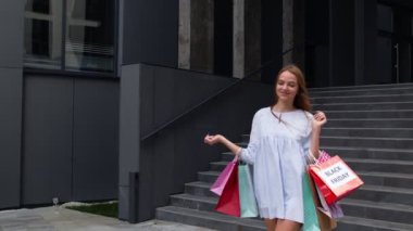 Alışveriş merkezinden alışveriş torbalarıyla yürüyen güzel bir kız, Kara Cuma günü satın almaktan memnun.
