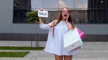 Güzel genç kız Kara Cuma yazısını gösteriyor, gülümsüyor, düşük fiyatlardan memnun görünüyor.