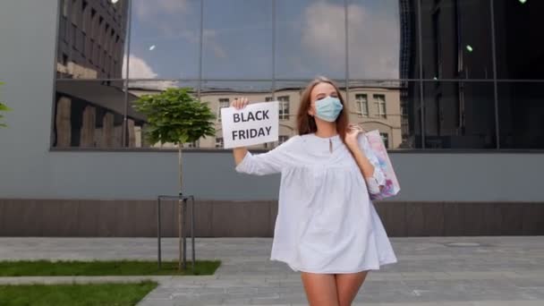 Ragazza in maschera protettiva con borse della spesa che mostrano iscrizione Venerdì nero durante coronavirus — Video Stock