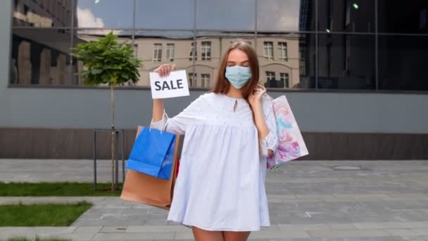 Fille dans un masque de protection avec des sacs à provisions montrant Vente inscription mot pendant la pandémie de coronavirus — Video