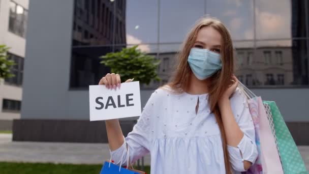 Девушка в защитной маске с пакетами с надписью Продается слово во время пандемии коронавируса — стоковое видео