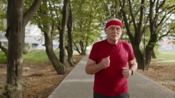 Senior oude man loopt, traint cardio in het park en het gebruik van bluetooth oortelefoons, luisteren muziek — Stockvideo
