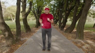 Park yerinde kıdemli bir adam koşuyor. Olgun koşucu antrenman yapıyor, müzik dinliyor.