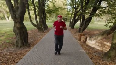 Yaşlı adam koşuyor, parkta kardiyo yapıyor bluetooth kulaklık kullanıyor, müzik dinliyor.