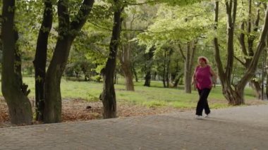 Yaşlı bir kadın parkta koşuyor ve akıllı saat kullanıyor. Bayan koşucu dışarıda kardiyo çalışıyor.