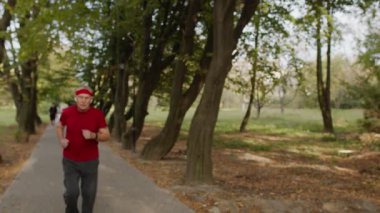 Yaşlı sporcu koştuktan sonra durur, akıllı saat kullanır, spor yaparken kalp atışlarını kontrol eder.